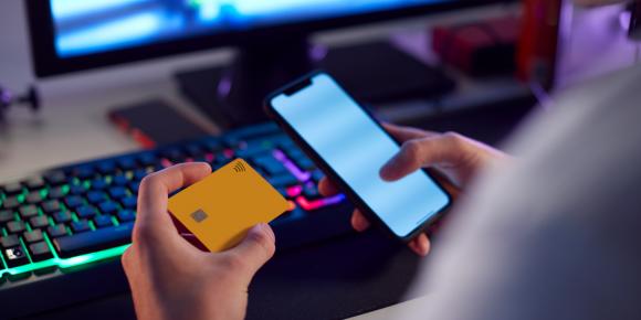 Un jeune qui paie pour un jeu vidéo. Informations sur les risques liés aux coûts cachés dans les jeux vidéo.